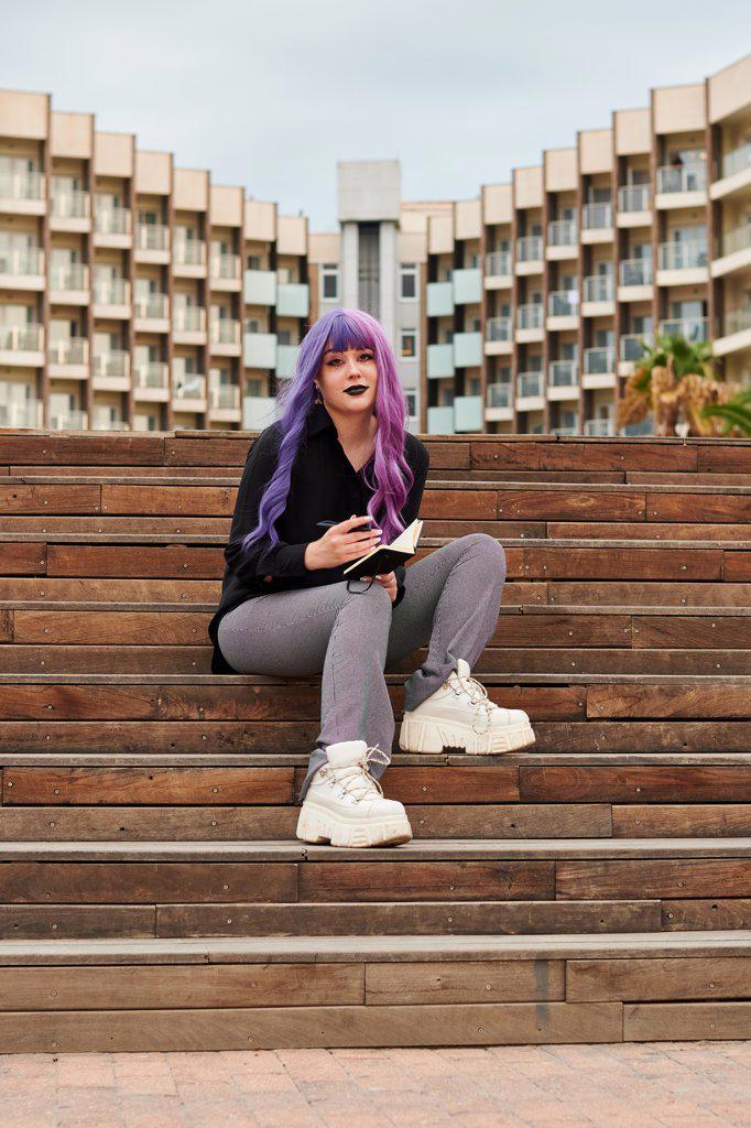 Non-binary person with a purple wig looks at camera on the street