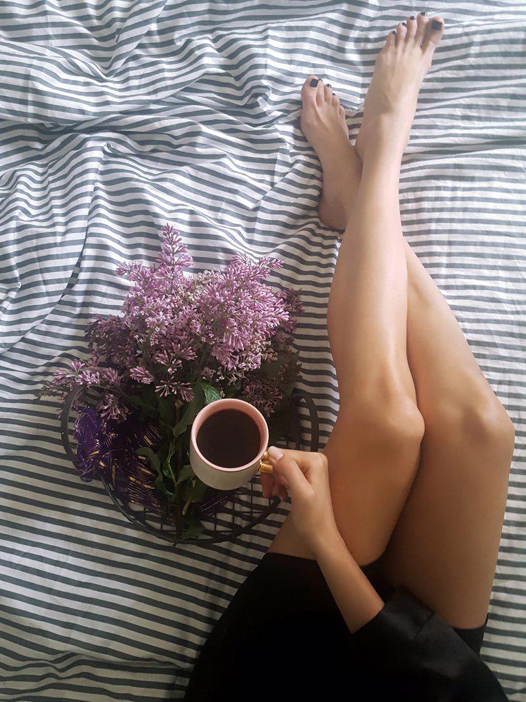 Woman slender legs on a striped sheet with lilacs and coffee