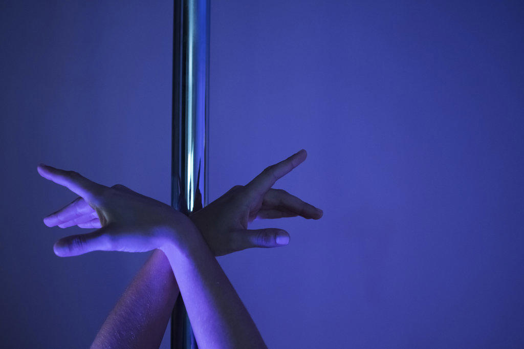 Detail of female athlete's hands posed on pole in pole dance studio