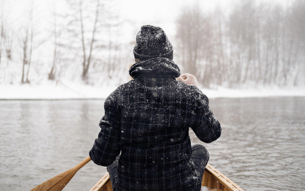 Person in a boat on a snowy river, view from behind
