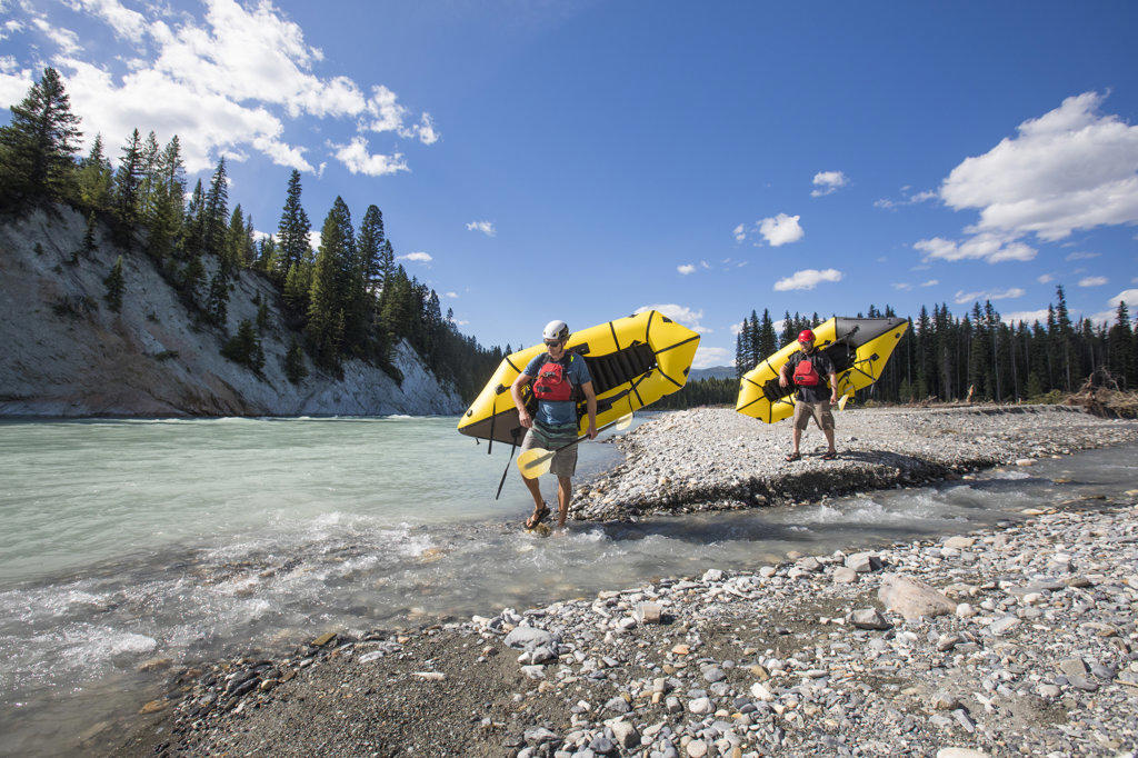 Paddlers carry yellow packrafts on shore to river put-in.