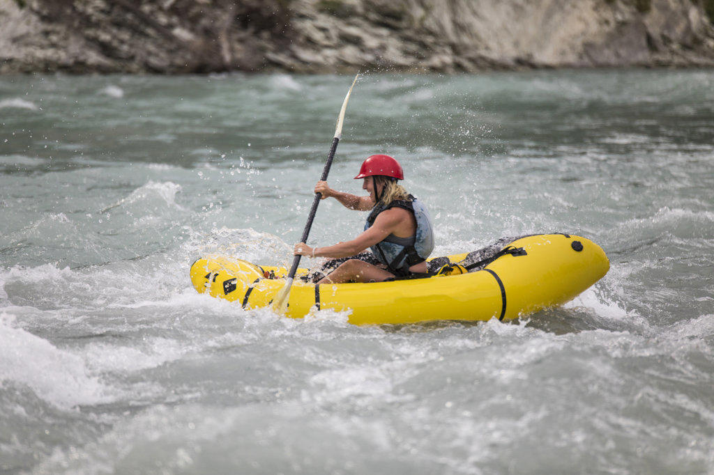 Side view of active fit woman packrafting through rapids.