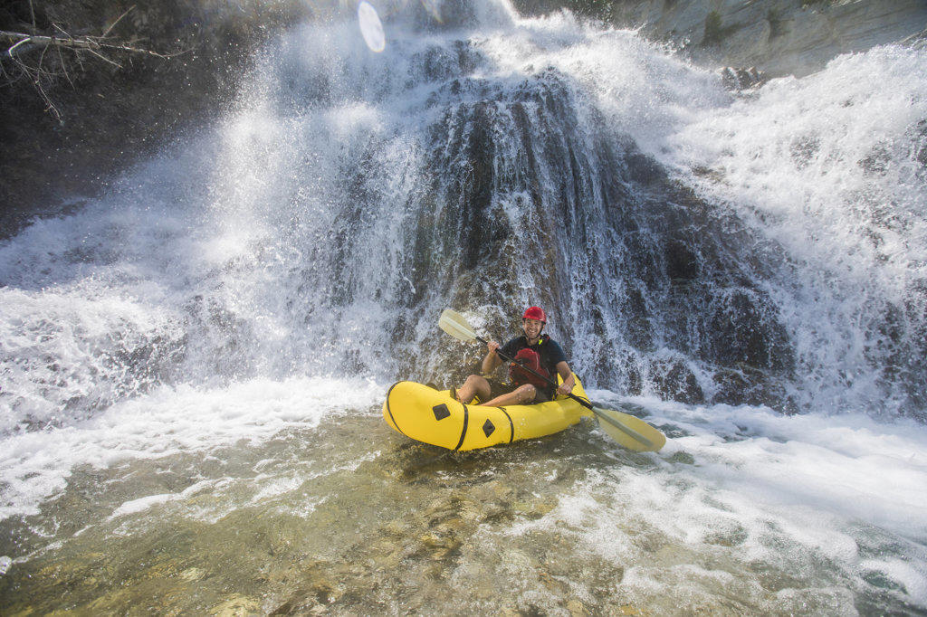 Adventurous man explores waterfall using a packraft.