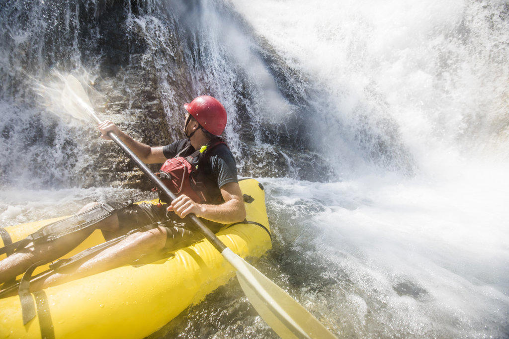 Paddler gets soaked while exploring river and waterfalls on raft.