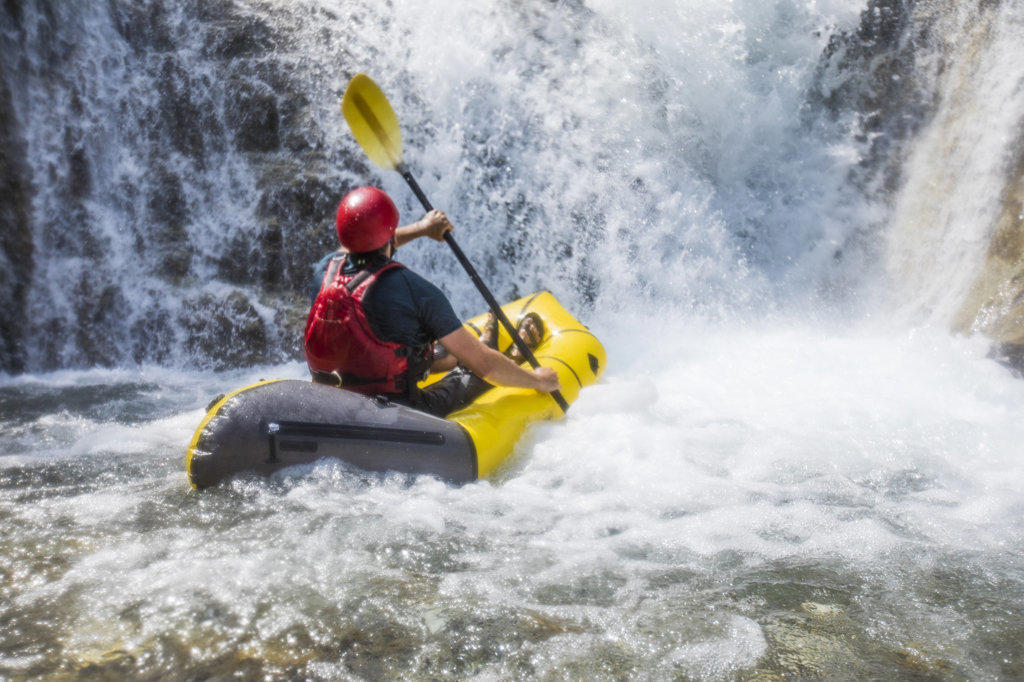 Man rafting on river below large waterfall in British Columbia Canada.