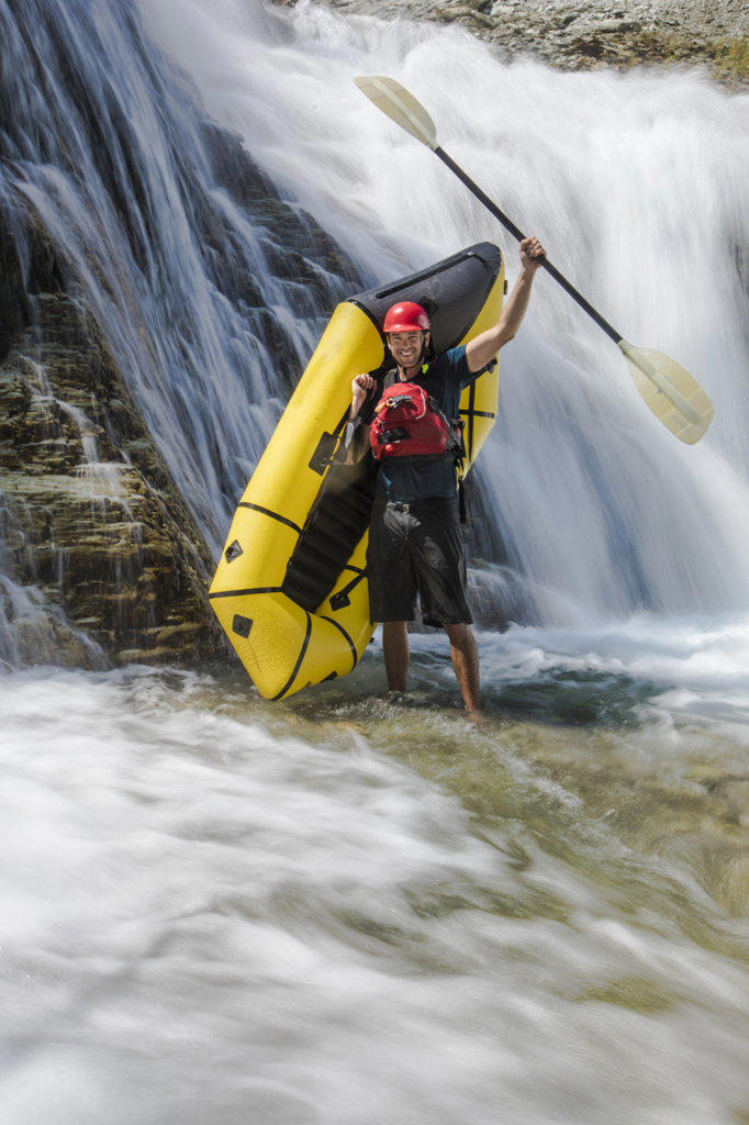 Paddler stands beside waterfall, raising paddle in the air.