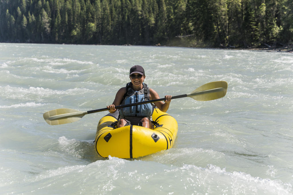 Attractive Fit active woman paddling packraft on river.