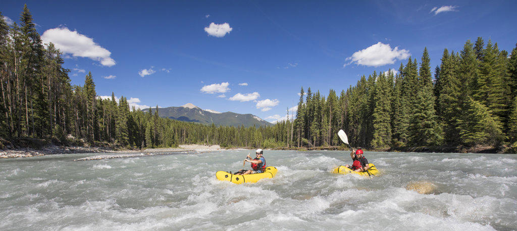 Panoramic view of two paddlers packrafting scenic river, B.C. Canada.