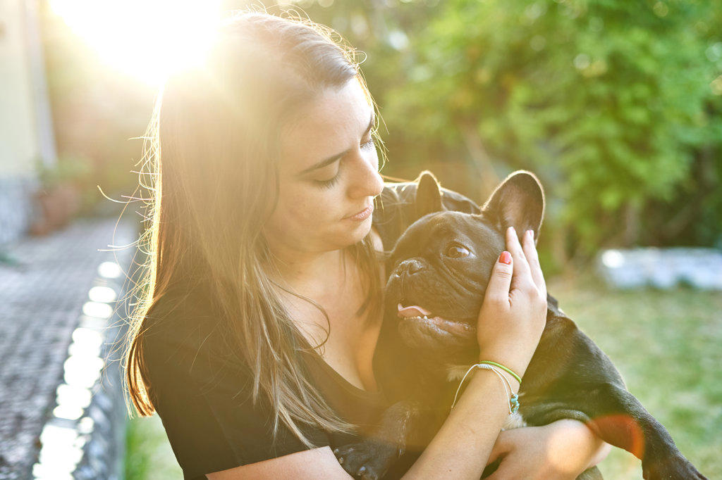 Young woman and her dog in the garden at sunset