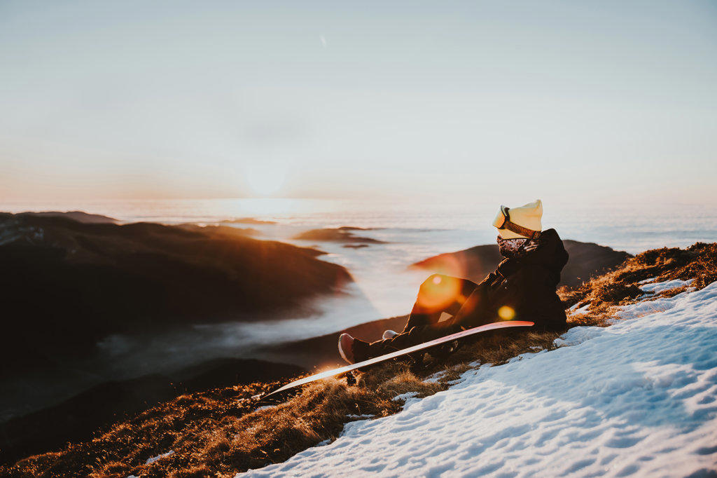 Snowboarder relaxing at sunrise on the mountain above clouds