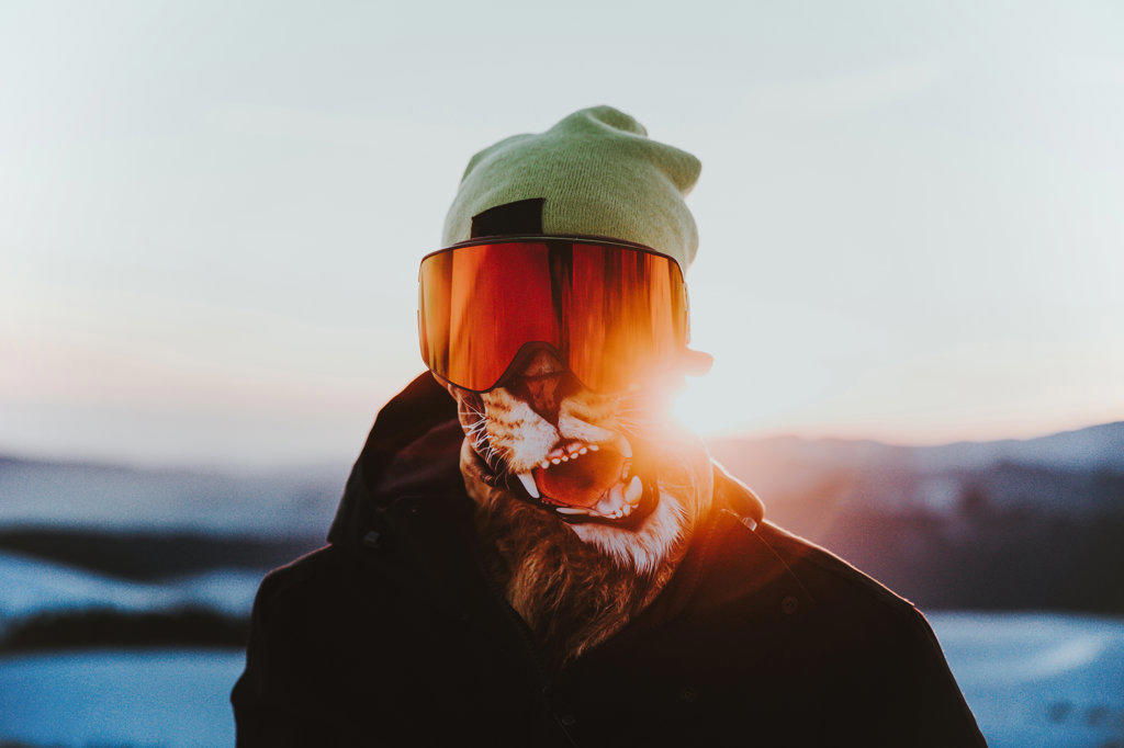 Athlete wearing buff goggles and snow jacket on the mountain at sunset
