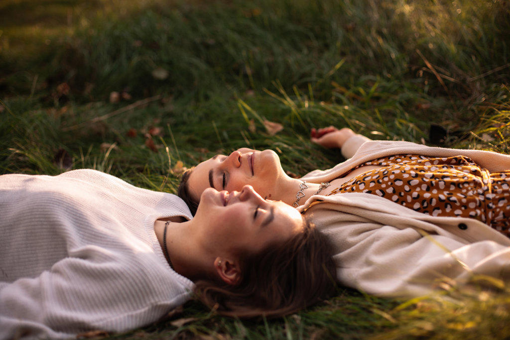 Happy lesbian couple smiling while lying on grass with eyes closed