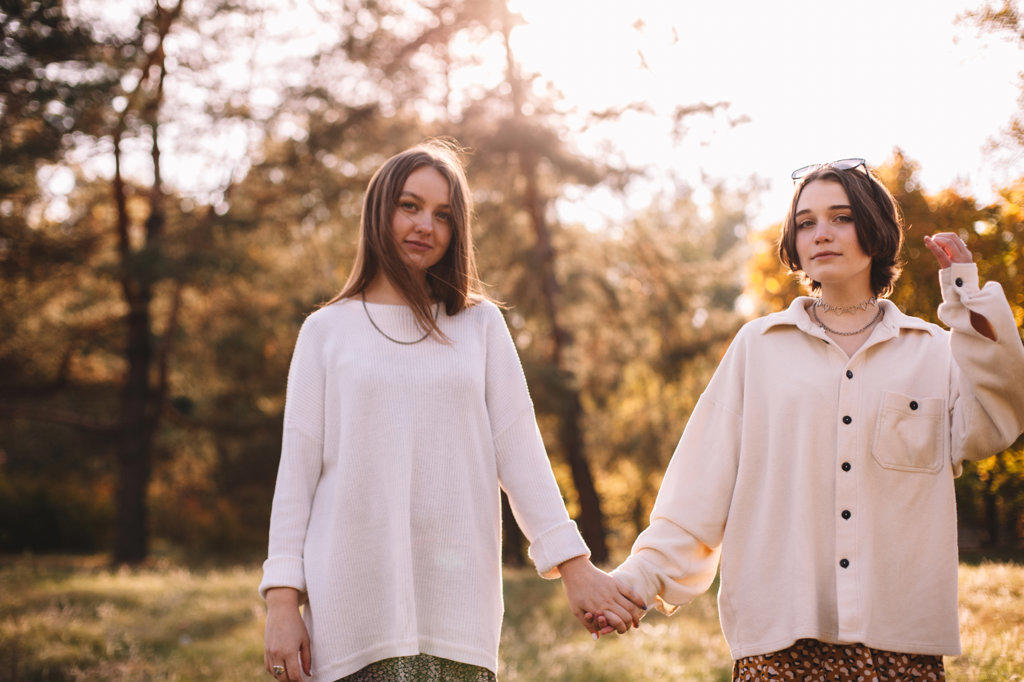 Two young women holding hands while standing in forest during autumn