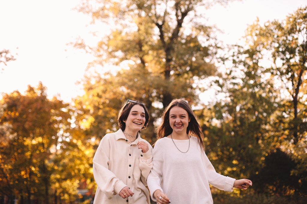 Two happy female friends smiling while walking in park during autumn