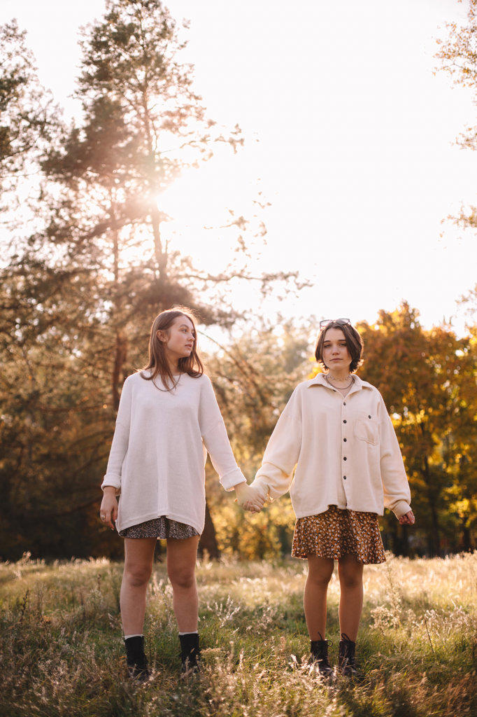 Lesbian couple holding hands while standing in forest during autumn
