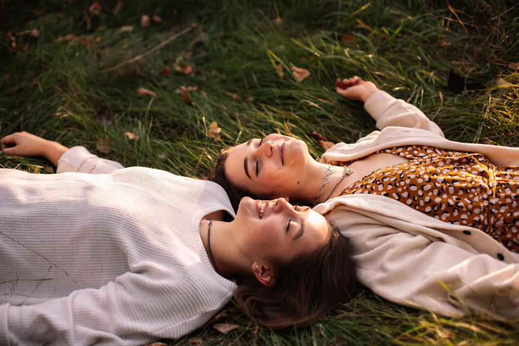 Two happy female friends smiling while lying on grass with eyes closed