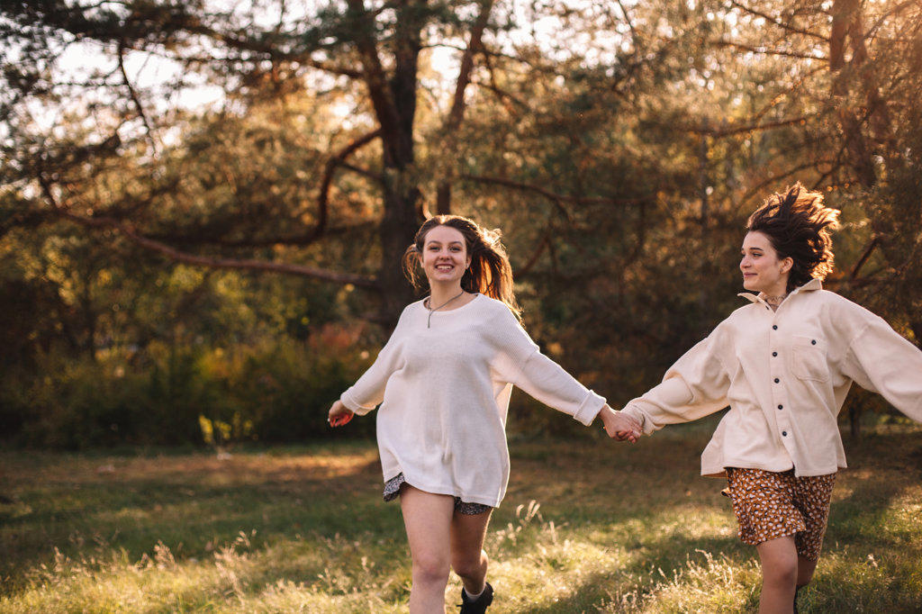 Two happy female friends holding hands while running in forest