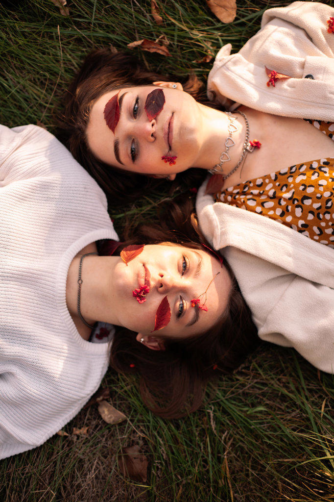 Two teenage girls with red leaves on faces lying on grass in autumn