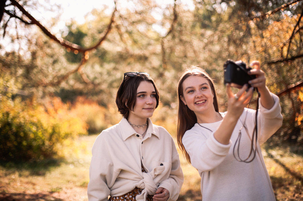 Happy female friends taking selfie standing in park in autumn