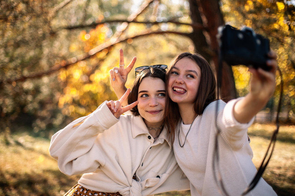 Happy teenage girls taking selfie standing in park in autumn