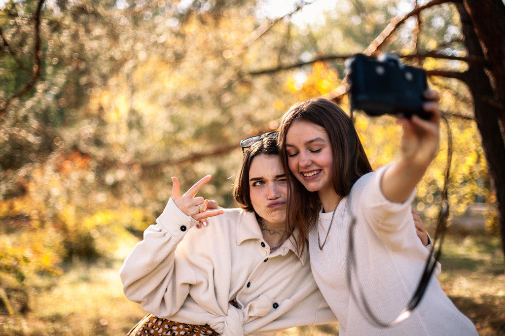 Happy girlfriends taking selfie standing in park in autumn