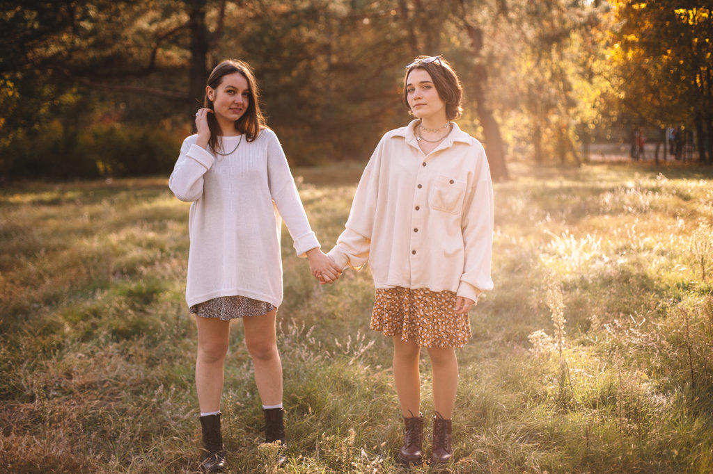 Two young women holding hands while standing in park during autumn