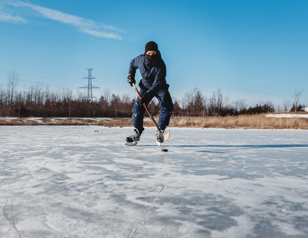 Teenage boy playing ice hockey on frozen pond on winter day in Canada.
