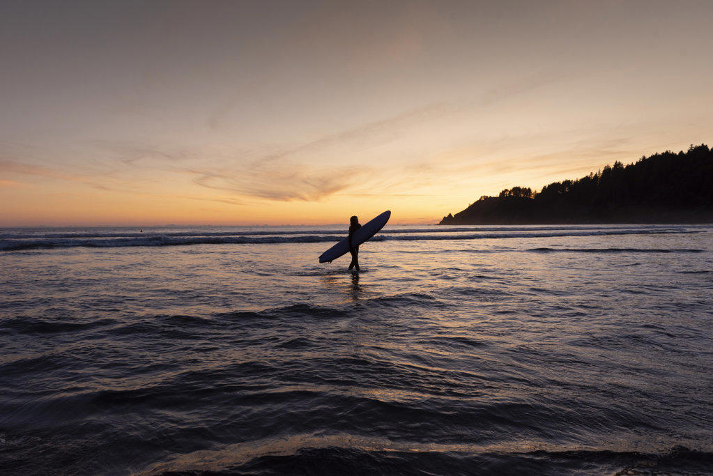 Silhouette of person carrying surfboard at Short Sands, Oregon
