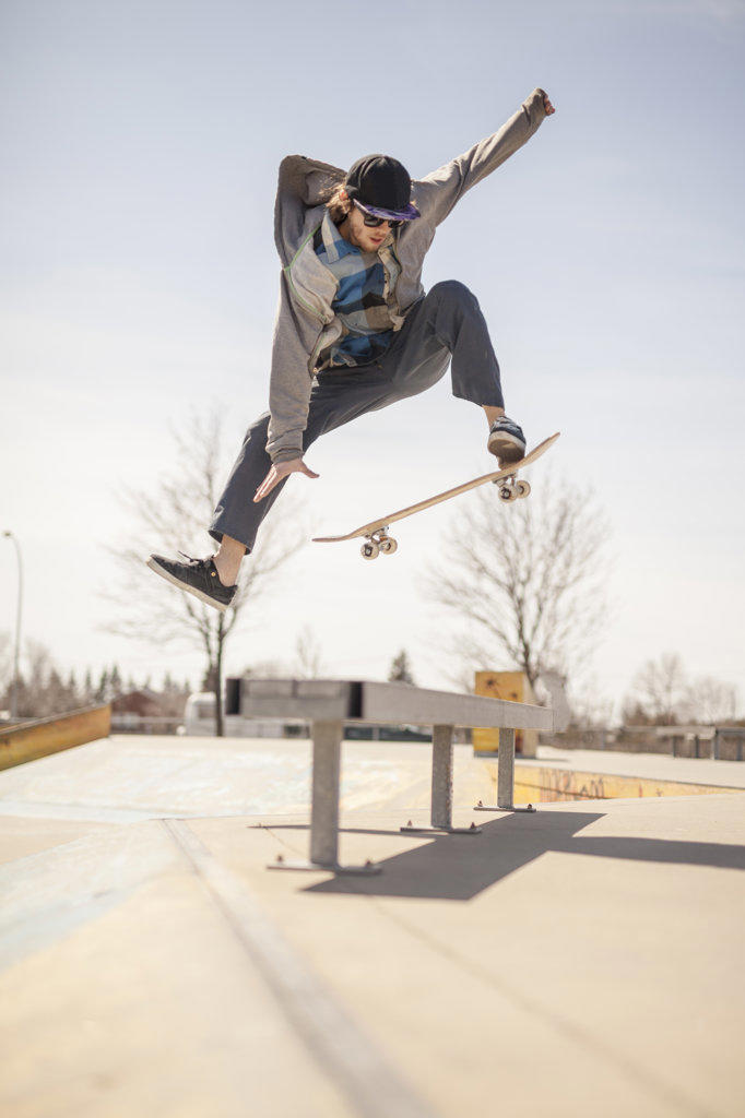 Young skateboard enthusiast in skatepark jumping over bench