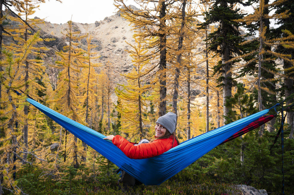 Female smiling in a hammock in a forest of larches during autumn