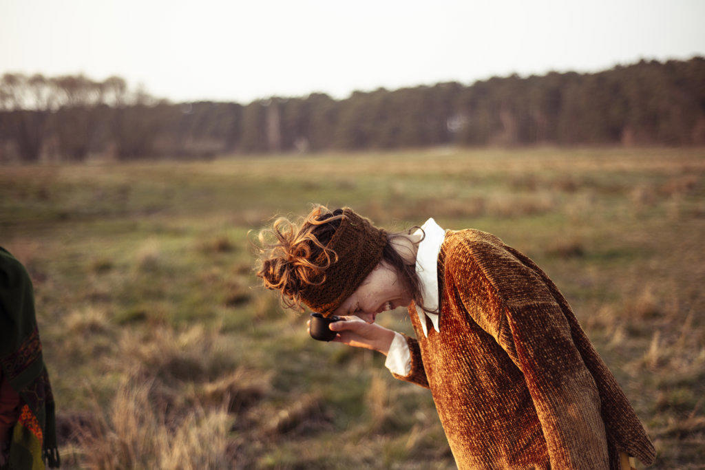 Female in earthy brown colours laughs drinking tea outside in field