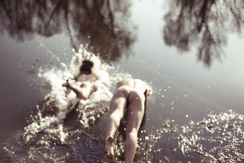Naked couple dive in natural water with reflection of trees