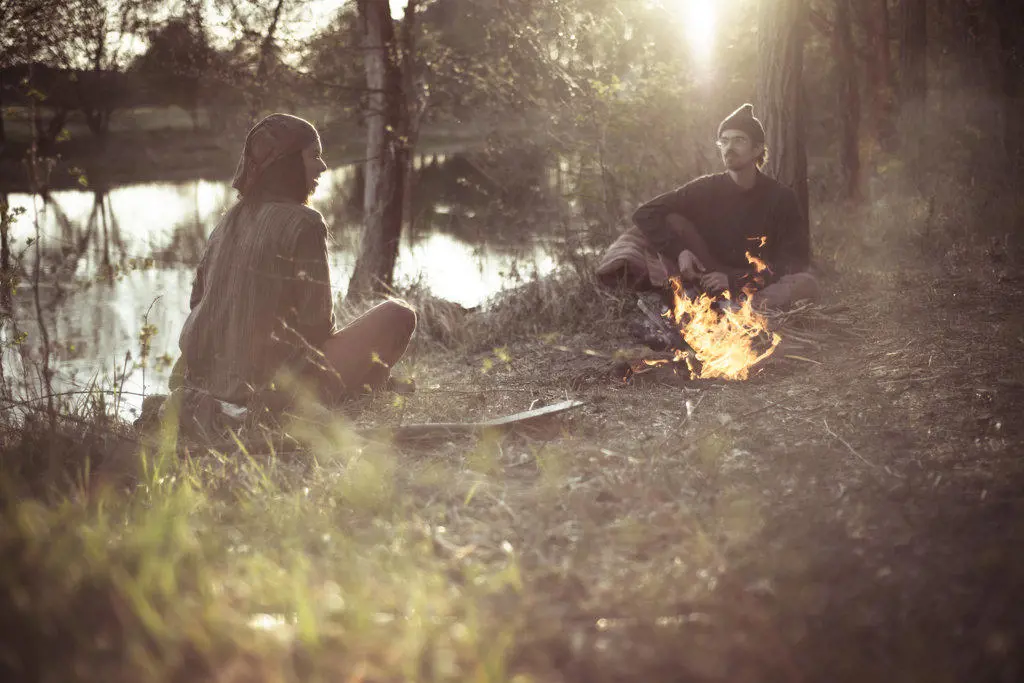 friends talk around fire in natural light by water