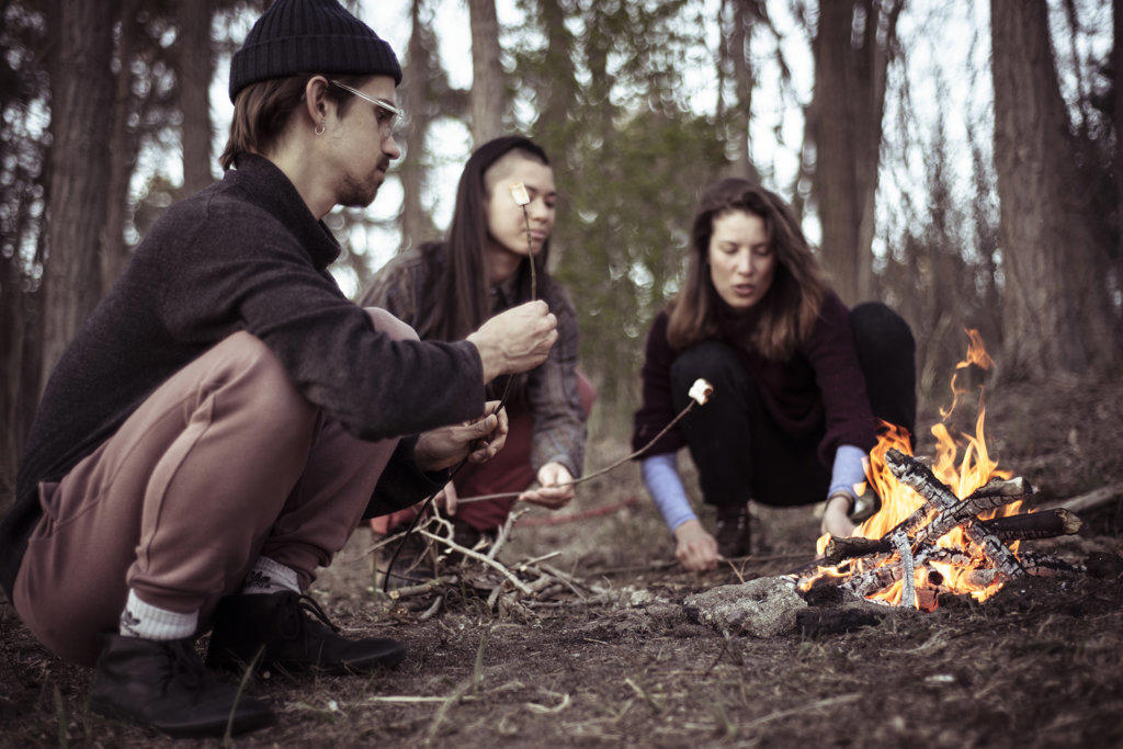 alternative friends gather and squat to roast marshmallows by fire