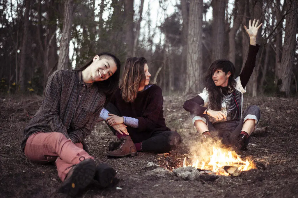 female friends chatting around campfire in forrest