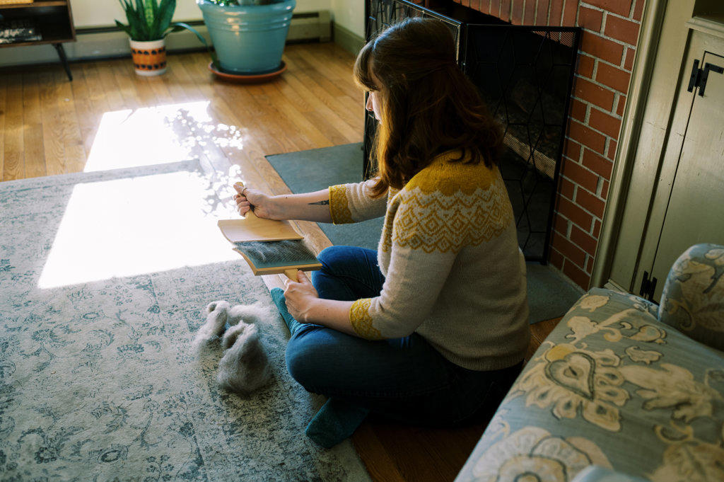 woman sitting in her living room brushing out wool roving
