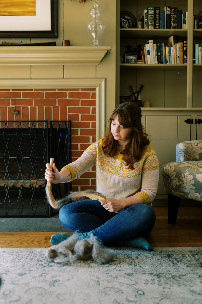 millennial woman brushing wool in front of fireplace at home