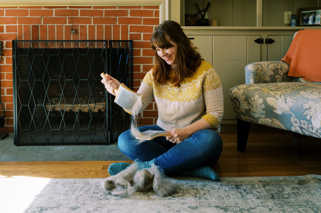 happy passionate millennial woman brushing wool roving by fireplace