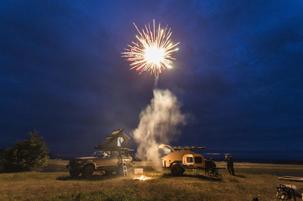Fireworks go off above a beach with camping trailer and camp truck