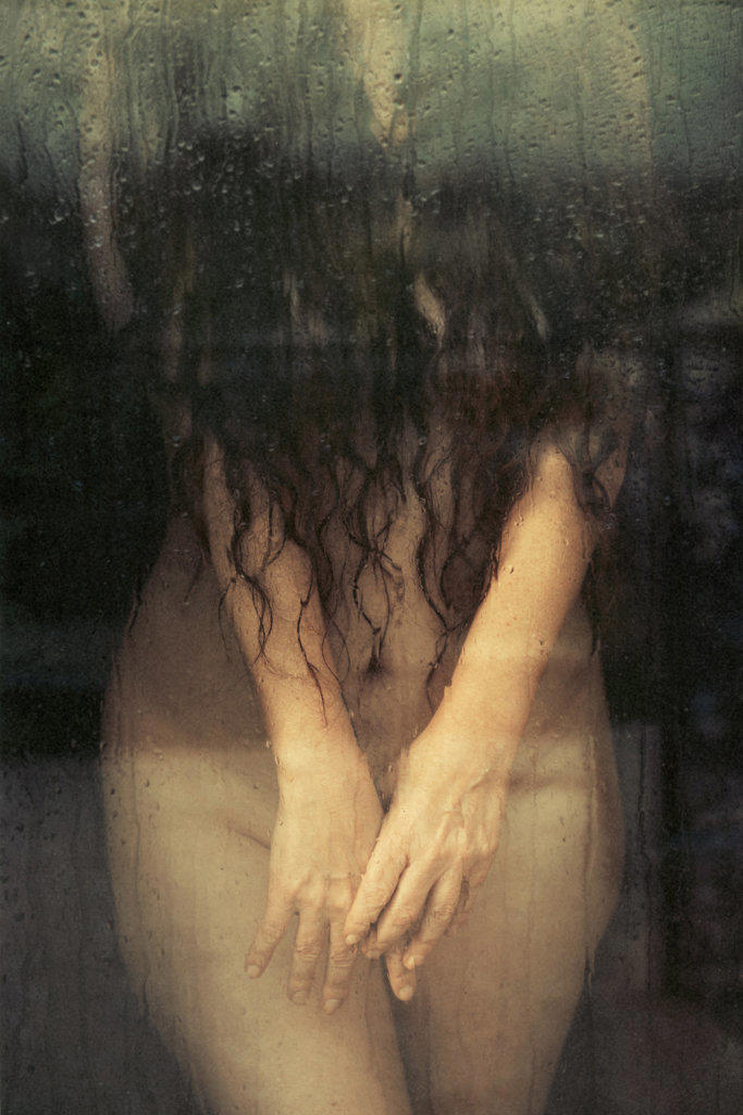 a woman standing behind glass covering her naked body with her hands