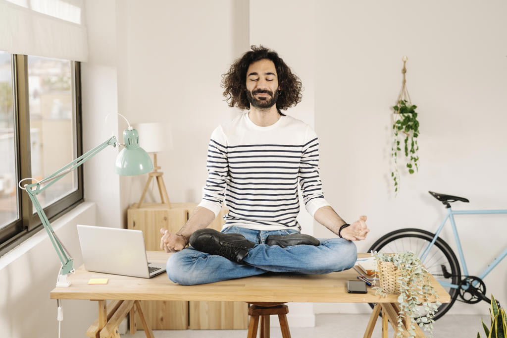 Young man meditating on desk at home
