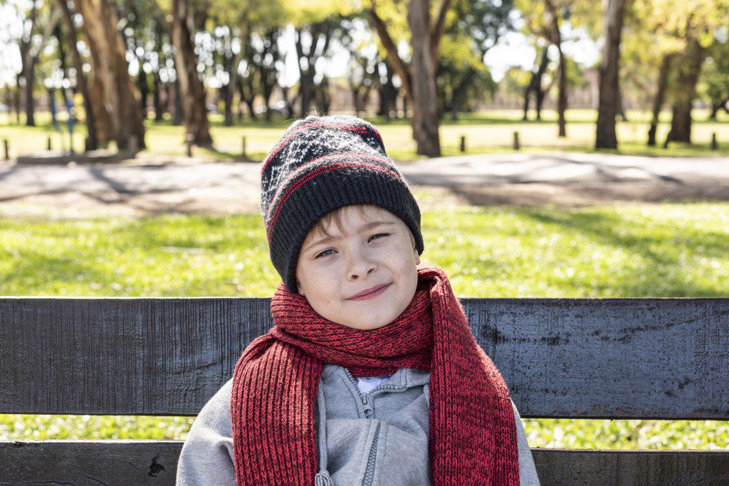 Kid sitting on a bench in the Park wearing a woolen Hat and scarf