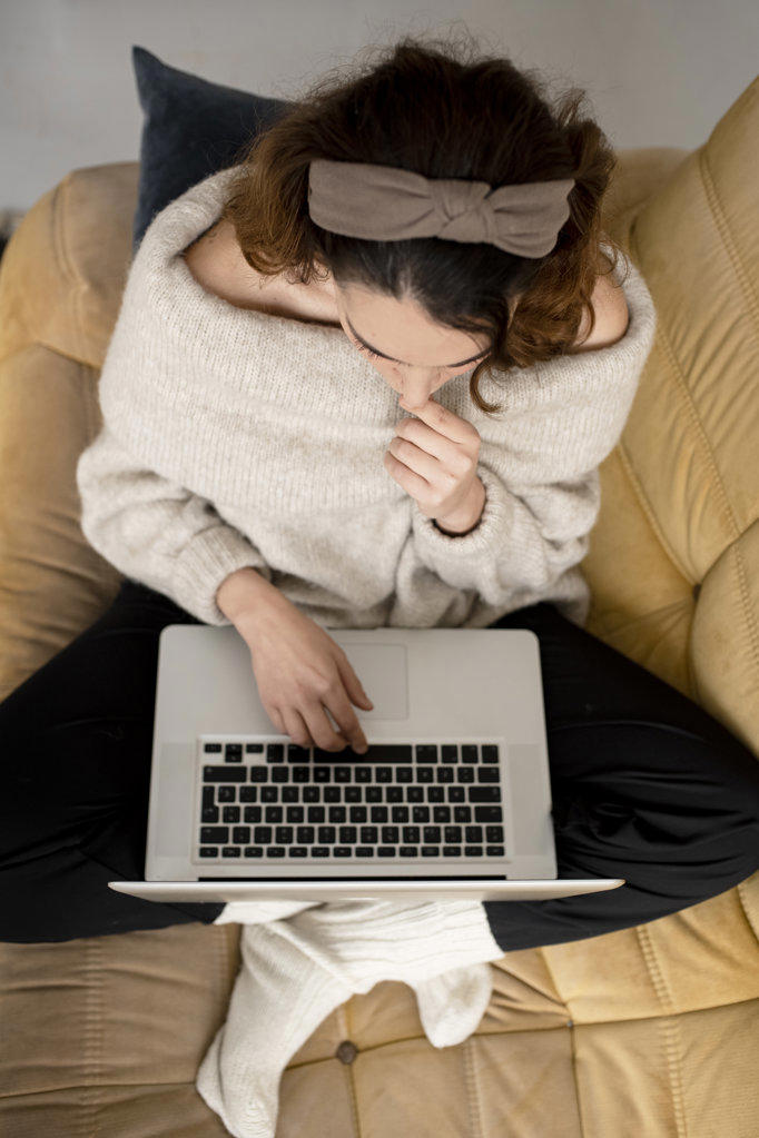 top view of young woman cross-legged sitting on sofa working on laptop