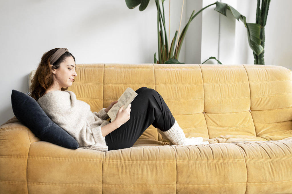 Beautiful smiling woman reading a book and lying on the sofa