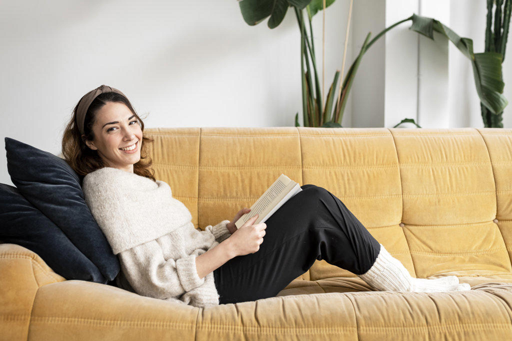 Beautiful smiling woman reading a book and smiling on the sofa
