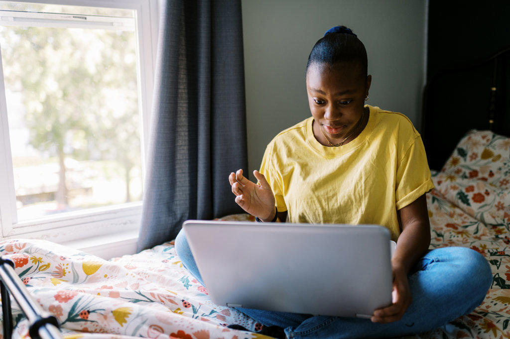 Young black teen sitting on her bed with her computer