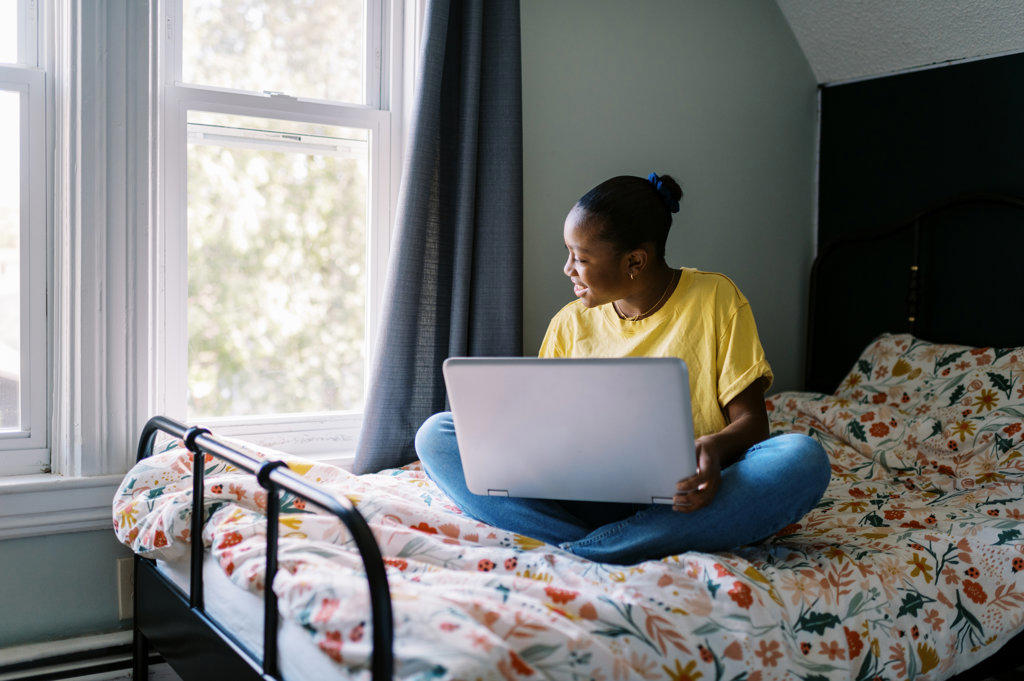 Young teenage girl in her room on her bed with laptop in her lap