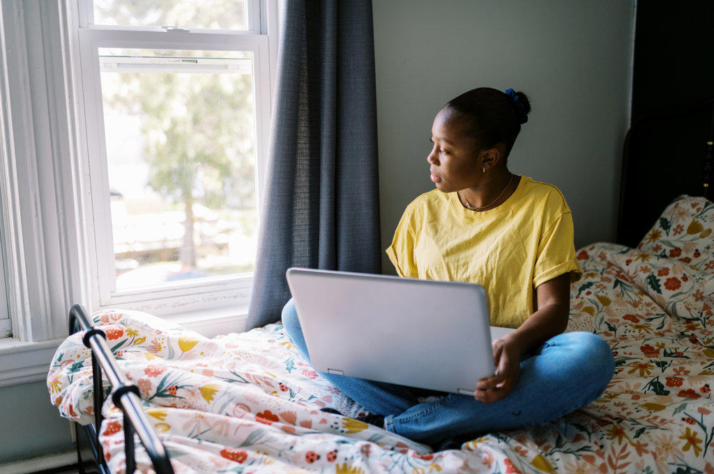 Young black girl sitting on her bed while working on computer