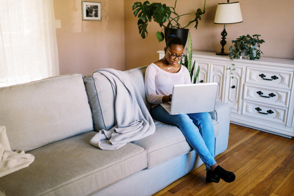 Young black teenage girl sitting on sofa with her computer