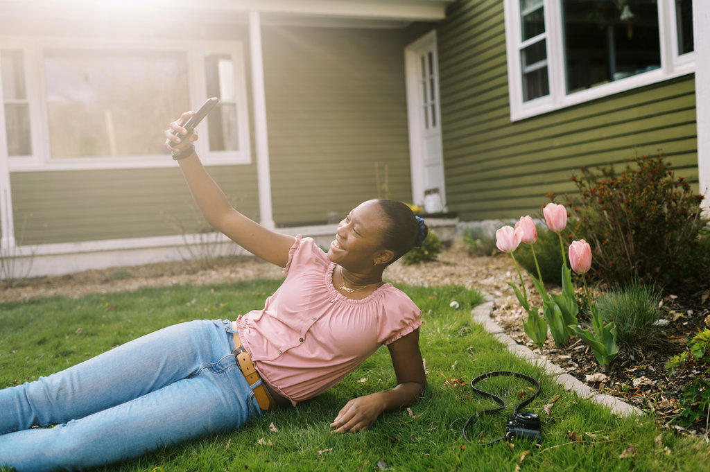 teenage girl lying in grass and taking a selfie with her phone